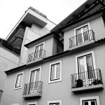 Edifício residencial português com varandas, visto de baixo, em tons de cinzento.