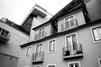 Edifício residencial português com varandas, visto de baixo, em tons de cinzento.