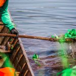 Trabalhador usando equipamentos de proteção remove plantas aquáticas de um lago.