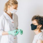 Profissional de saúde prepara uma vacina para uma paciente numa unidade clínica.
