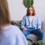 Jovem conversa com uma psicóloga durante uma sessão de psicoterapia em um consultório iluminado.