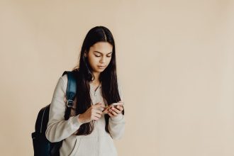 Adolescente com mochila usa um smartphone num ambiente interior minimalista.