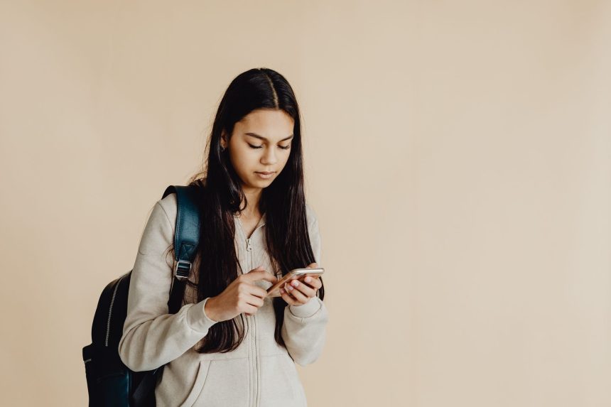 Adolescente com mochila usa um smartphone num ambiente interior minimalista.